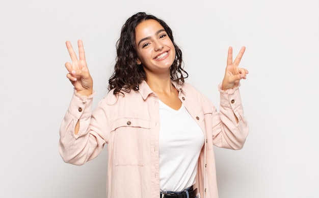 Bastante joven sonriendo y mirando feliz, amigable y satisfecho, gesticulando victoria o paz con ambas manos