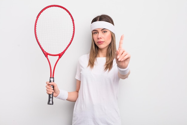 Bastante joven sonriendo con orgullo y confianza haciendo el concepto de tenis número uno