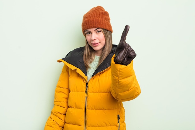 Bastante joven sonriendo con orgullo y confianza haciendo el número uno. concepto de clima frío