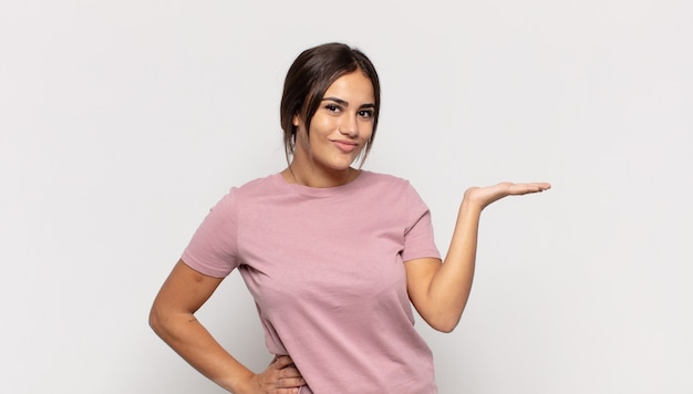 Bastante joven sonriendo, sintiéndose confiada, exitosa y feliz, mostrando concepto o idea en el espacio de la copia en el lateral