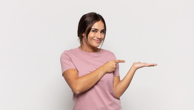 Bastante joven sonriendo, sintiéndose feliz, despreocupada y satisfecha, señalando el concepto o la idea en el espacio de la copia en el lateral