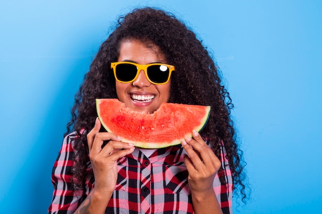 Bastante joven sosteniendo una rebanada de sandía delante de su cara. Retrato de sonriente niña afroamericana aislada saludable y feliz