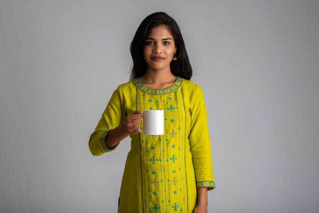 Bastante joven con una taza de té o café posando en la pared gris