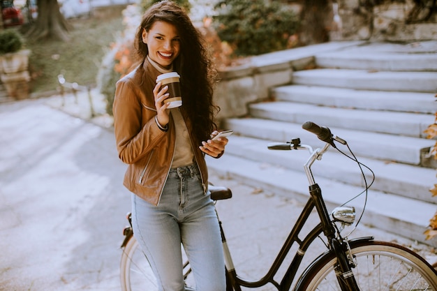 Bastante joven con teléfono móvil beber café para ir en bicicleta el día de otoño