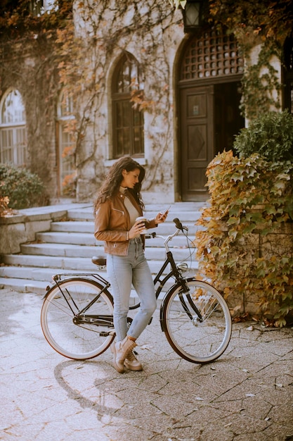 Bastante joven con teléfono móvil beber café para ir en bicicleta el día de otoño