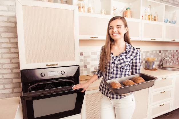 Foto bastante joven tomando una bandeja de horno con pan horneado del horno