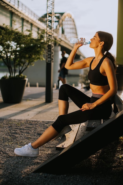 Bastante joven tomando un descanso durante el ejercicio al aire libre y bebiendo agua