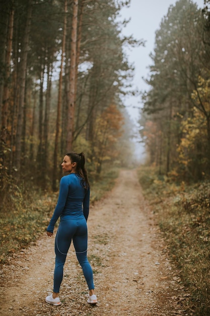 Foto bastante joven tomar un descanso durante el ejercicio al aire libre en la pista forestal en otoño