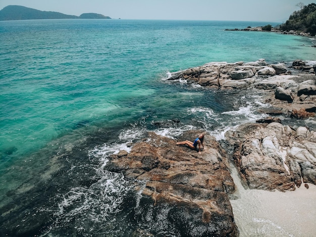 Bastante joven en un traje de baño azul tomando el sol en las rocas durante la marea alta. Concepto de vacaciones de verano