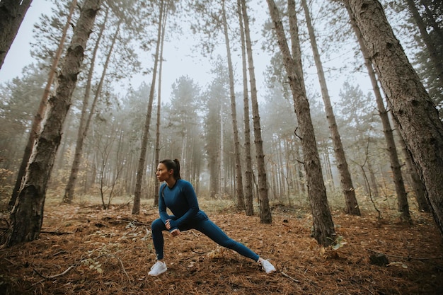 Bastante joven en traje de pista azul que se extiende antes de entrenar en el bosque de otoño