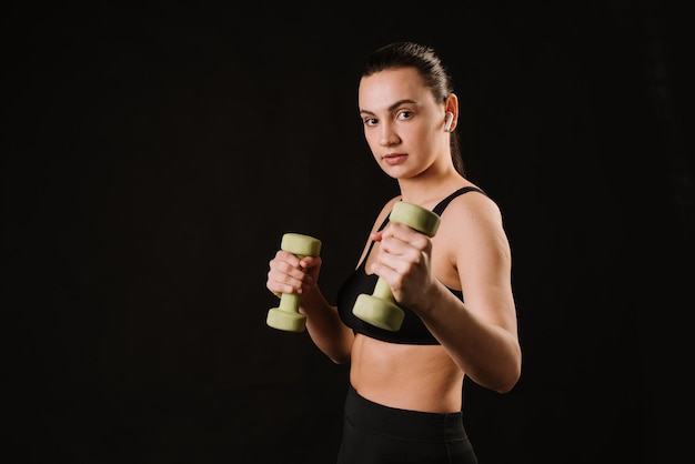 Bastante modelo de fitness haciendo ejercicios con pesas sobre fondo negro. copia espacio