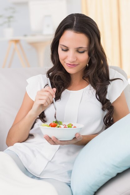 Bastante morena comiendo ensalada en el sofá