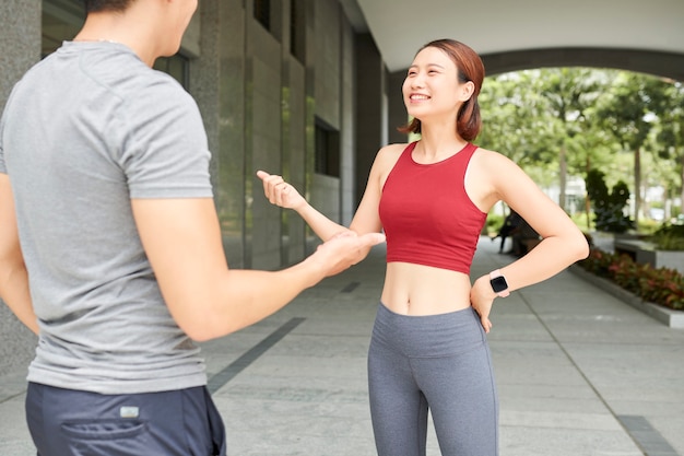 Bastante sonriente joven deportista asiática hablando con su novio antes de trotar al aire libre