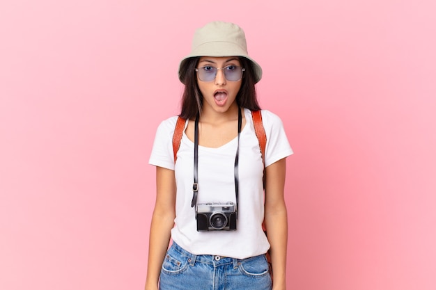 Bastante turista hispana mirando muy conmocionado o sorprendido con una cámara de fotos y un sombrero