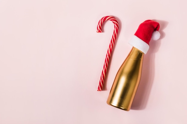 Bastão de doces de Natal e champanhe dourado no chapéu de Papai Noel em fundo rosa Conceito mínimo de férias