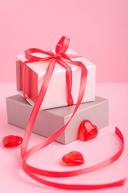 Bastelgeschenkboxen mit Schleife aus rotem Band auf pastellrosa Hintergrund mit Herzdekor