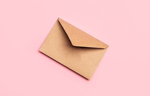Basteln Sie Papierpostumschlag für Briefe auf einem rosa Hintergrund. Minimalistischer Stil, Draufsicht, Korrespondenzkonzept.