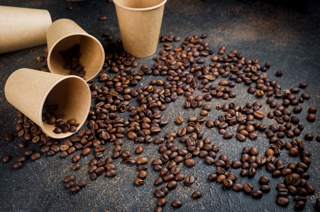 Basteln Sie Pappbecher für Kaffee und Kaffeebohnen auf dunklem Betonhintergrund. Das Konzept der Heißgetränke zum Mitnehmen, Belebendes Frühstück.