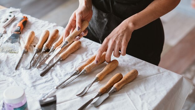 Bastelset auf Tisch arrangiert. Schnitz- und Modellierwerkzeuge. Handwerksfrau mit Meißel. Wahl. Kunstwerk in Bearbeitung.