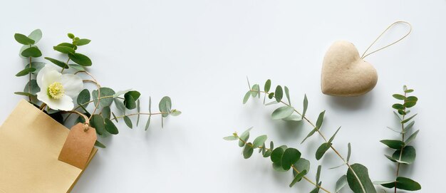 Basteltasche mit winterlichem eukalyptus und weißer helleborus-blume. panoramabanner. braunes papieretikett, kopierraum. winterwohnung lag mit immergrünen zweigen und winterrosenblüte auf weißem hintergrund