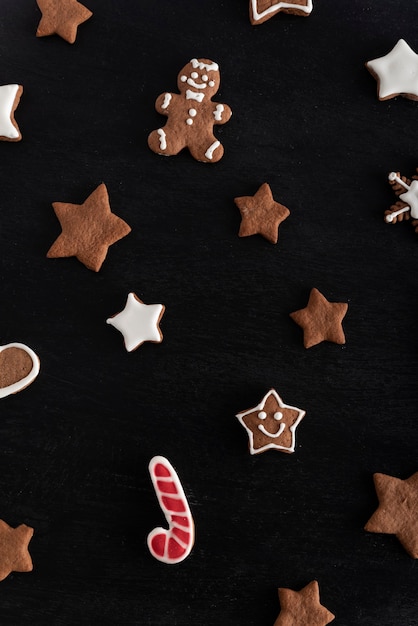 Bastón de caramelo de jengibre y galletas de estrellas sobre fondo negro. Repostería tradicional. Marco vertical.