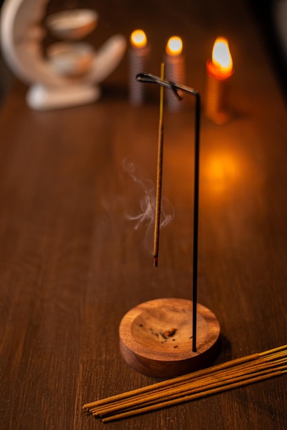 El bastón de incienso fuma en un soporte de madera en un fondo oscuro el humo de la aromaterapia mientras quema incienso