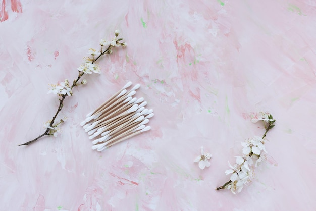 Bastoncillos de algodón de bambú ecológicos sobre fondo rosa con flores blancas de primavera