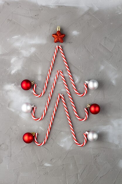 Bastones de caramelo en forma de árbol de Navidad con estrella y bola sobre fondo gris. Concepto abstracto de vacaciones de año nuevo.