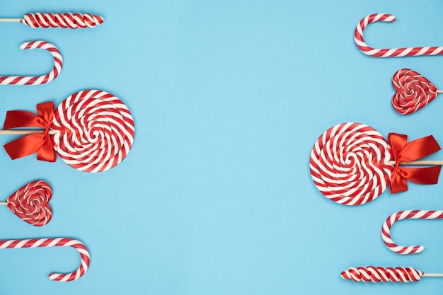 Bastones de caramelo de Navidad a rayas rojas y piruletas sobre fondo azul.