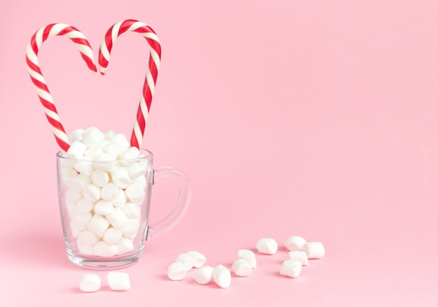 Bastones de caramelo Whitered corazón y malvavisco en taza sobre fondo rosa Concepto feliz día de San Valentín