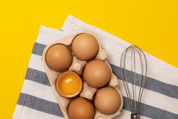 Bata ou batedeira com ovos de galinha marrons em uma cesta ecológica em fundo amarelo