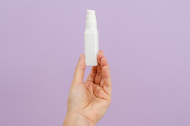 Batalla de crema cosmética en mano de mujer sobre fondo lila claro Concepto de belleza Tubo de embalaje para productos cosméticos