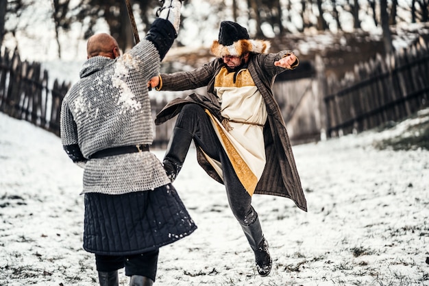 Batalla de dos guerreros armados con armas que luchan con espadas en la nieve.