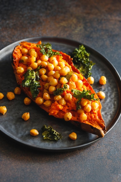 Batata al horno rellena de garbanzos y col rizada crujiente en un plato negro Sabroso plato vegano para la cena o el almuerzo