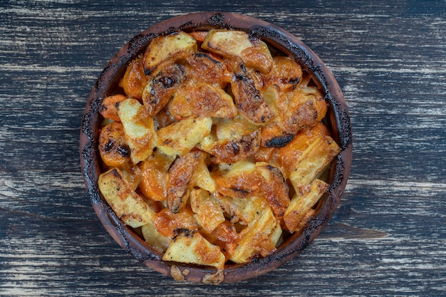 Batata assada e cenoura com queijo na mesa de madeira, close-up. Tigela de cerâmica com fundo de fatias de batata e cenoura, vista superior