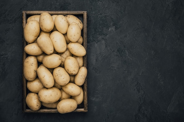 Batata Batatas orgânicas cruas frescas em caixa de madeira sobre fundo escuro de pedra