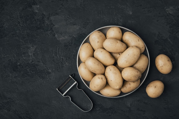 Batata Batatas orgânicas cruas frescas em tigela com descascador em fundo escuro de pedra