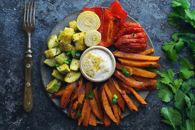 Batata-doce assada no forno caseiro com tomate cebola pimenta vermelha e molho na mesa de pedra escura conceito de alimentação saudável vista superior