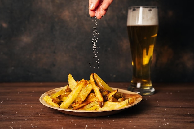 Batata frita com um copo longo de cerveja em fundo rústico escuro