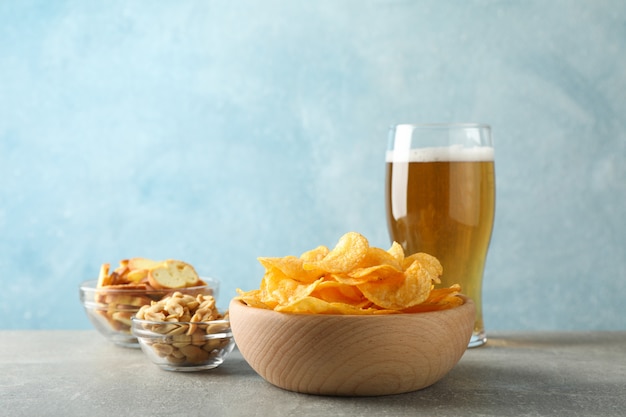 Batata frita em uma tigela e um copo de cerveja. Petiscos de cerveja, nozes de cerveja na mesa cinza em azul, espaço para texto