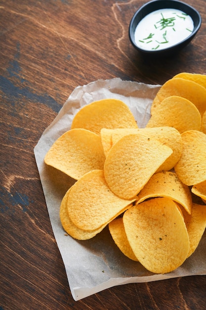 Batata ondulada Chips Fast food Batatas fritas crocantes tigela preta cerâmica com molho de creme azedo e cebolas em suporte de madeira na velha mesa de cozinha fundo de madeira Tradição americana Hot BBQ Vista superior