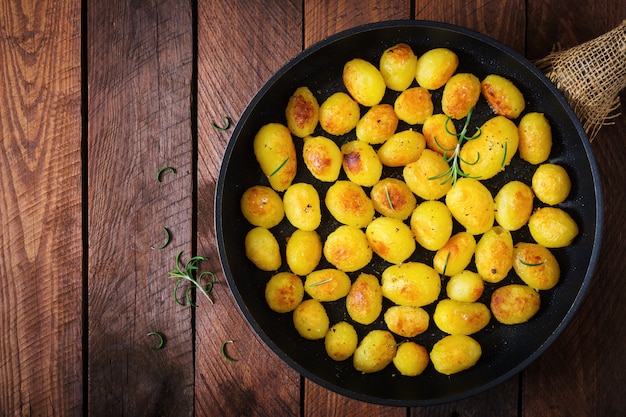 Batatas assadas com alecrim e pimenta em uma frigideira com fundo de madeira. Vista do topo