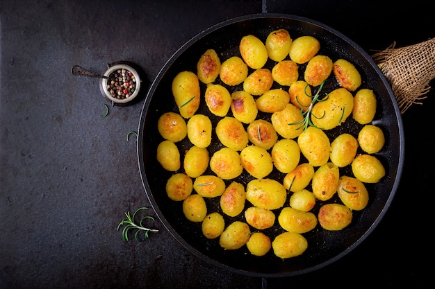 Batatas assadas com alecrim e pimenta em uma frigideira em fundo preto. Vista do topo