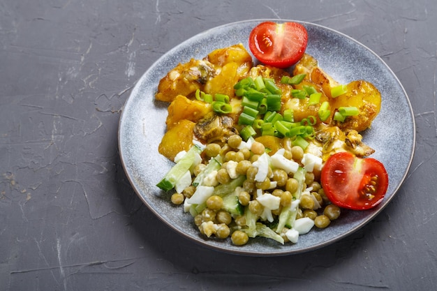 Foto batatas assadas com queijo e cogumelos guarnecido com tomate cereja polvilhado com cebolinha em um prato em um espaço de cópia de fundo cinza