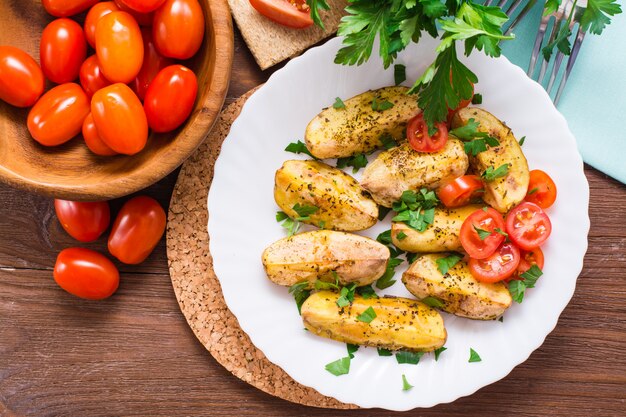 Batatas assadas com tomates maduros e ervas frescas em um prato.