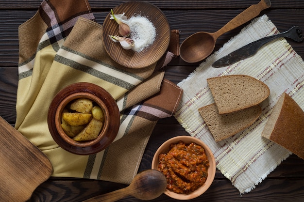 Batatas assadas em uma panela de barro, pão e molho sobre uma mesa de madeira