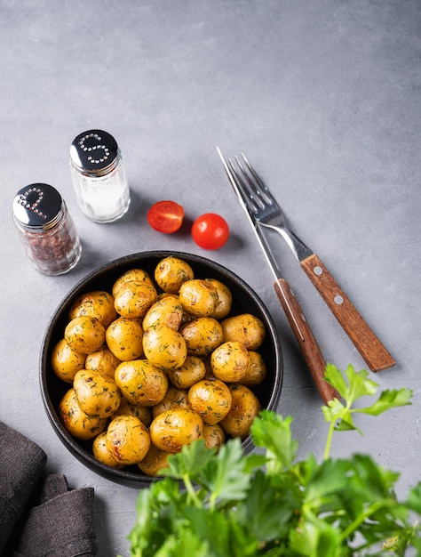 Batatas assadas jovens em uma panela preta com tomates e ervas em um fundo azul