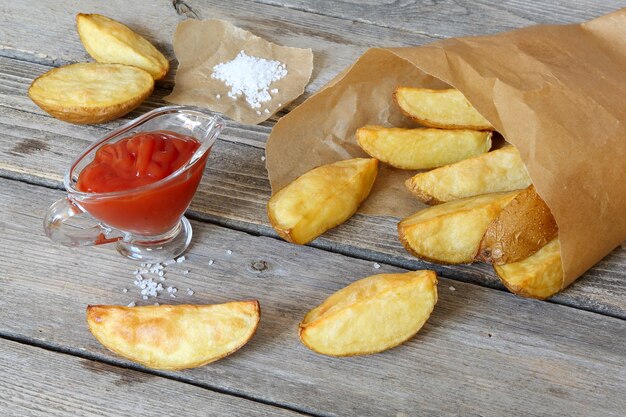 Batatas assadas num saco de papel e ketchup na mesa de madeira