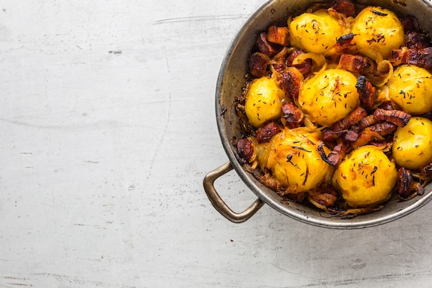 Batatas. Batatas assadas com bacon, cebola e salsichas na mesa de concreto branca.