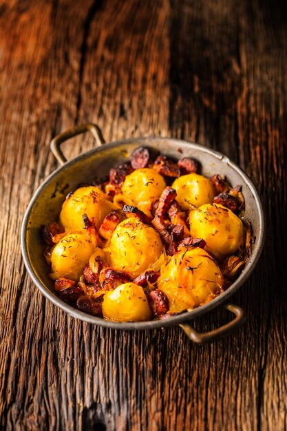 Batatas. Batatas assadas com bacon, cebola e salsichas na velha mesa de carvalho.